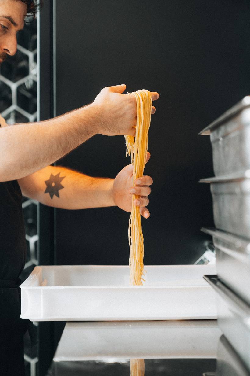 Een kok legt verse spaghetti in de bak